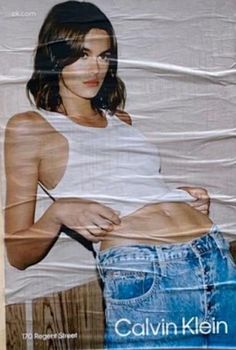 a woman in white shirt and jean shorts standing next to a poster with her stomach exposed