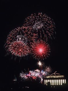 fireworks are lit up in the night sky over a building and water with lights on it