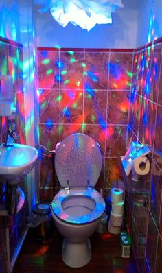 a bathroom with colorful lights on the wall and toilet in the center, next to a sink