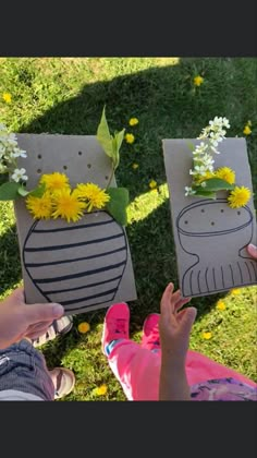 two people are holding up small vases with flowers in them on the grass outside