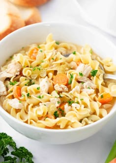 a white bowl filled with chicken noodle soup on top of a table next to bread