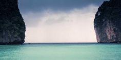 two large rocks sticking out of the ocean next to each other in front of an overcast sky