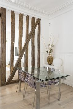 a glass table with metal legs in front of a wall made of wooden beams and branches