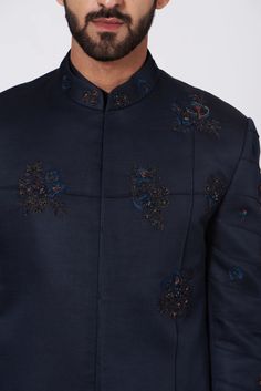 Midnight blue bandhgala with floral motifs and pintuck details. Designer Blue Bandhgala, Elegant Blue Nehru Jacket For Semi-formal Occasions, Designer Blue Bandhgala For Festive Occasions, Designer Blue Nehru Jacket, Designer Fitted Bandhgala With Buttons, Designer Embroidered Bandhgala For Semi-formal Events, Designer Fitted Bandhgala With Stand Collar, Designer Embroidered Bandhgala For Semi-formal Occasions, Designer Nehru Jacket With Floral Embroidery