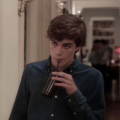 a young man holding a drink in his hand and looking at the camera while standing in a hallway