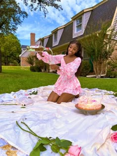 a woman in a pink dress sitting on a blanket with a cake and roses around her