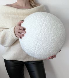 a woman is holding a large white ball in her right hand and wearing black leather pants