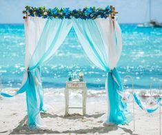 an outdoor wedding setup on the beach with blue and white draping, flowers and ribbons