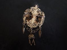 "This handsome, flickering brooch features detailed filigree and cannetille work. The brooch is quite dimensional with raised and dangling ornament. It was probably made in Portugal or Spain. The security clasp works just fine. The brooch is in good shape with some surface wear to the gilding. It is 6.7cm (2 5/8\")long X 3.2cm (1 1/4\")wide. It weighs 10g." Antique Pendant Brooch With Intricate Design, Antique Brooch With Intricate Pendant Design, Ornate Engraved Brooch, Ornate Pendant Brooch For Ceremonial Occasions, Ornate Gold Locket Brooches, Victorian Gold Pendant Brooches, Antique Brooches With Intricate Design For Ceremonial Use, Antique Ceremonial Brooches With Intricate Design, Antique Yellow Gold Filigree Brooches