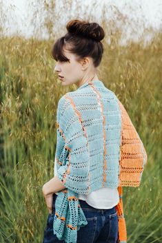 a woman standing in tall grass wearing a crocheted shawl