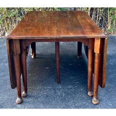 an old wooden table with three legs and two smaller tables on top, sitting in front of some bushes