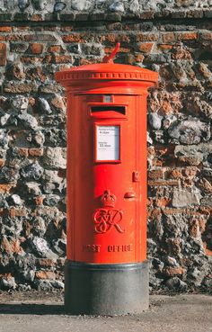 an orange post box sitting in front of a brick wall