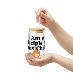 a person holding a glass jar with an orange and black design on the bottom that says, i am a disciple o jesus christ