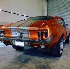 an orange mustang parked in a garage next to a white car with stripes on it