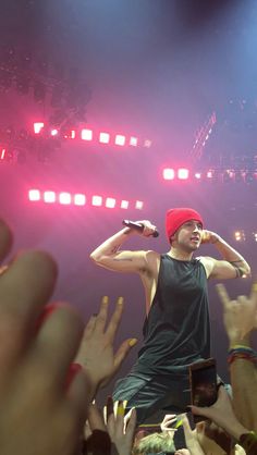 a man standing on top of a stage with his hands in the air and holding a microphone to his ear