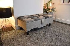 a grey ottoman sitting on top of a carpeted floor next to a lamp and mirror