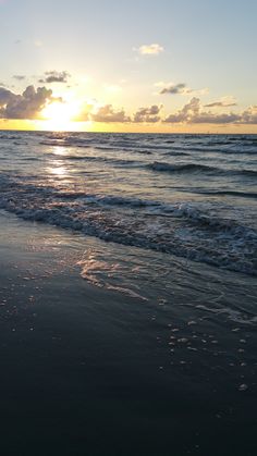 the sun is setting over the ocean with waves coming in to shore and some clouds