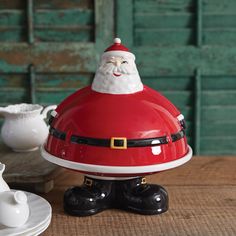 a santa clause figurine sitting on top of a wooden table next to white dishes