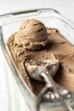 two scoops of ice cream sit in a glass dish with a spoon next to it