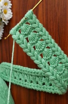 a green crochet piece sitting on top of a wooden table next to flowers