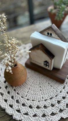 a small house sitting on top of a doily next to a potted plant