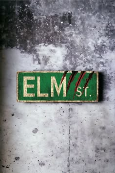 a green street sign mounted to the side of a cement wall that says elm st