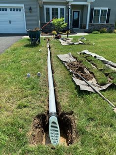 a drain in the middle of a yard next to a house with a large pipe sticking out of it