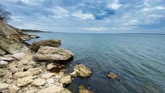 the water is calm and blue with some rocks on the shore in front of it