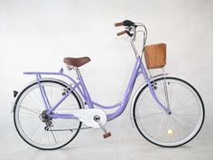 a blue bicycle with a basket on the front wheel and seat is parked against a white wall