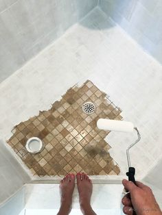 a person is using a paint roller to paint the floor in a bathroom with tiled walls