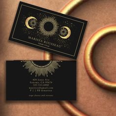 two business cards sitting on top of each other in front of a circular object with gold rings around it