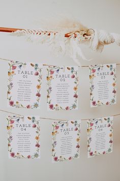 wedding seating cards hanging from a string on a wall with flowers and feathers attached to it