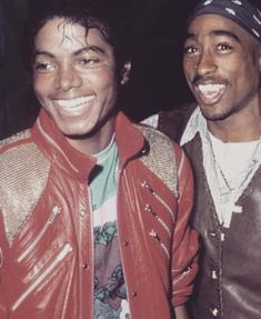 two men are smiling and posing for a photo together, one is wearing a red leather jacket