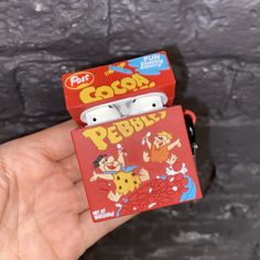 a hand holding a small red box with some cartoon characters on it