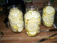 three jars filled with sliced lemons sitting on top of a wooden table next to a knife