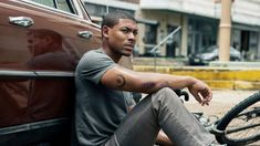 a man sitting on the ground next to a parked car with his bike in front of him