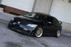 a black car with gold rims parked in front of a garage door and another car behind it