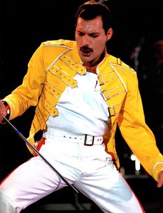 a man in yellow jacket and white pants performing on stage with microphone to his side