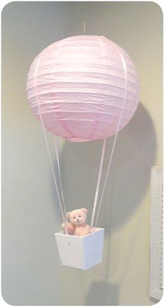 a teddy bear in a box suspended from the ceiling with a pink ballon attached to it