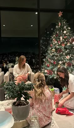 three women sitting around a table with a christmas tree in the background