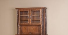 a wooden bookcase with glass doors on the top and bottom shelf, against a beige wall