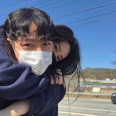 a man and woman wearing face masks on the side of the road in front of a car