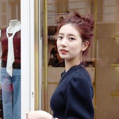 a woman is walking past a store window with her hand in her pocket and looking at the camera