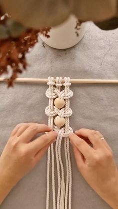 a woman is working on a piece of art with white string and wood beading