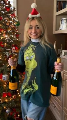 a woman holding two bottles of champagne in front of a christmas tree with a grin face on it