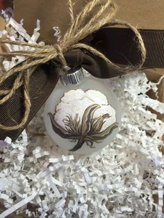 a white ornament sitting on top of shredded paper next to a brown ribbon