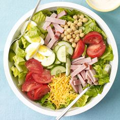 a salad with ham, lettuce, tomatoes, cucumbers and cheese