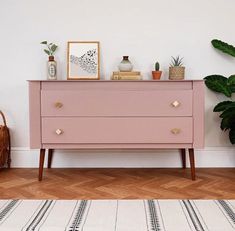 a pink dresser sitting next to a potted plant on top of a wooden floor