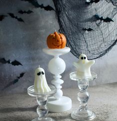 two halloween candles with ghost faces on them in front of a spooky net