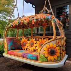 a swing bed with sunflowers on it in front of a house and trees